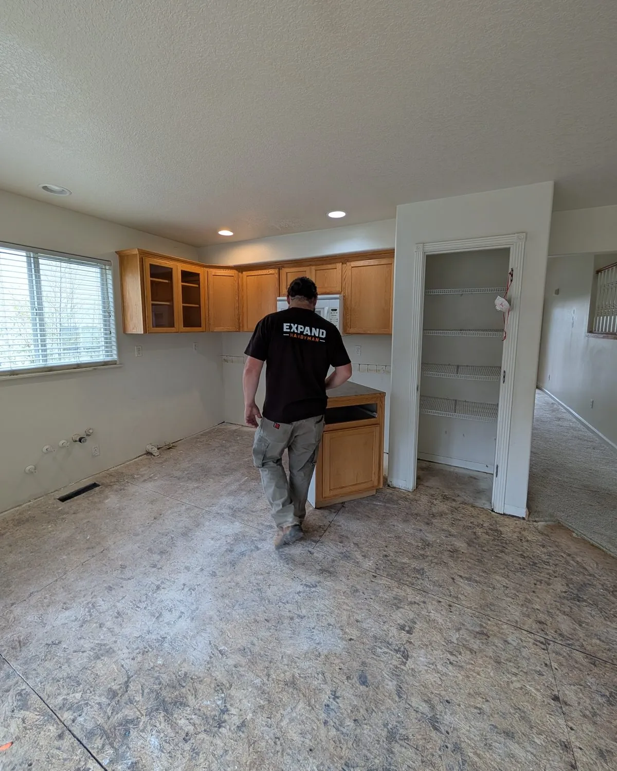 An Expand Handyman crew member walking through an empty kitchen with oak cabinets.
