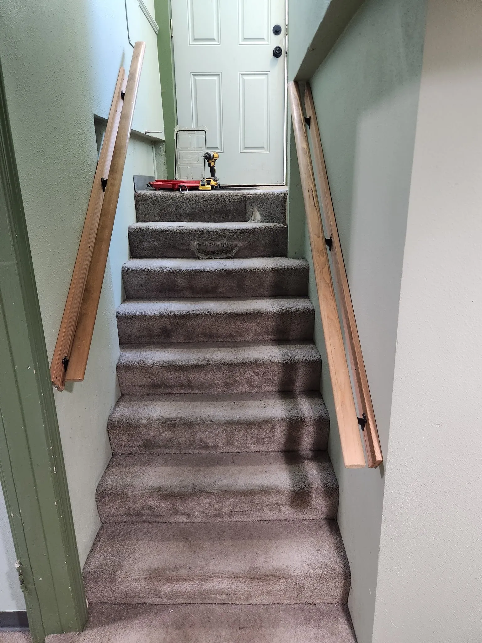 Narrow carpeted stairway with new wood handrails on both walls