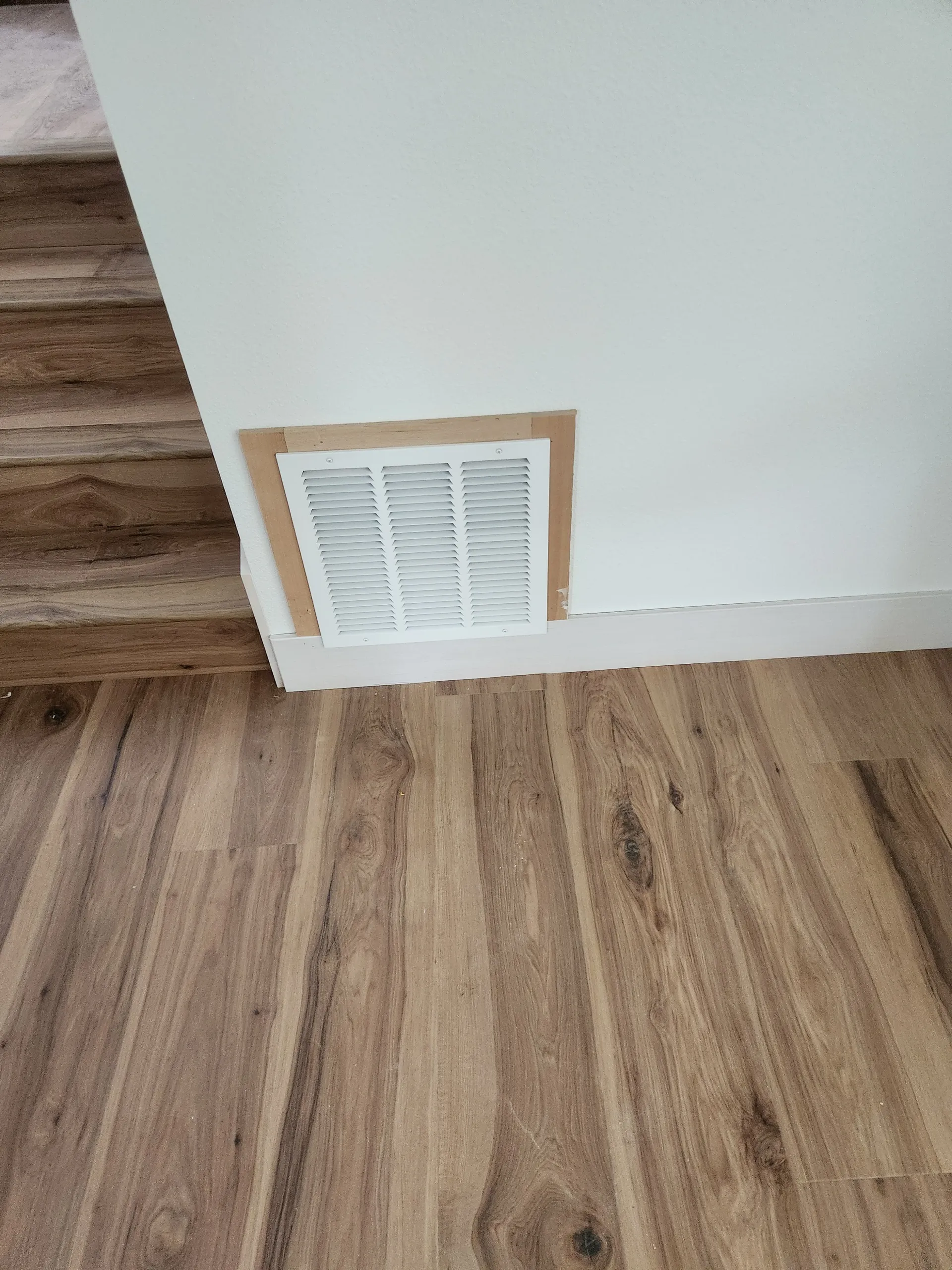 Wall vent framed in wood above new baseboard and flooring
