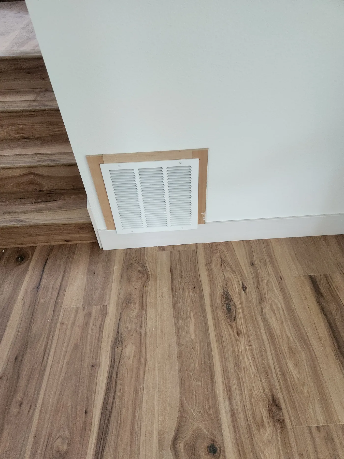 Wall vent framed in wood above new flooring